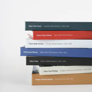 A stack of missionary books showing the foil-stamped spines with each missionary's name and mission
